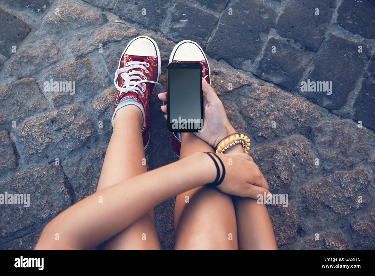 teenager girl sitting with mobile phone in hand, in ancient stone floor Stock Photo