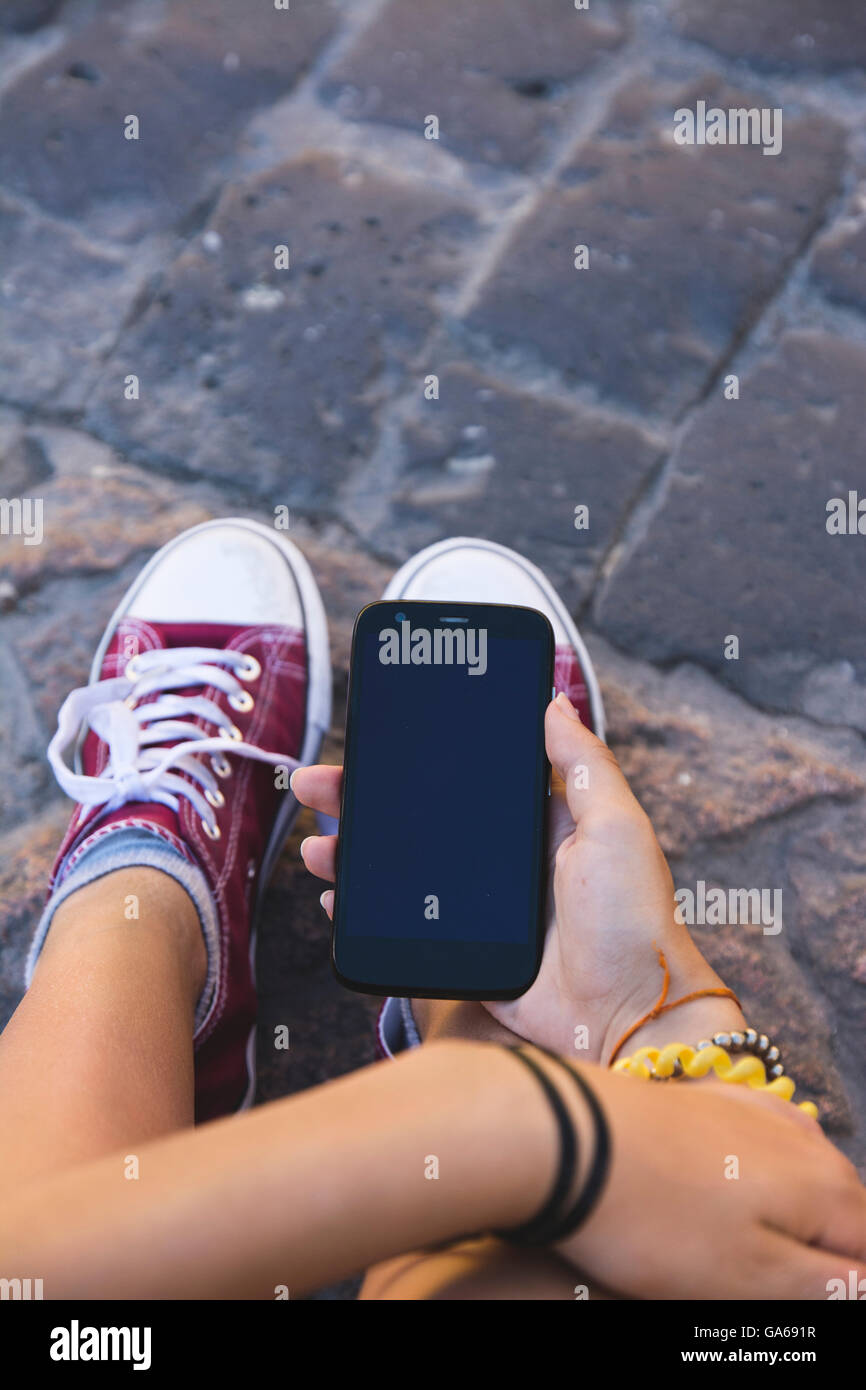 teenager girl sitting with mobile phone in hand, in ancient stone floor Stock Photo