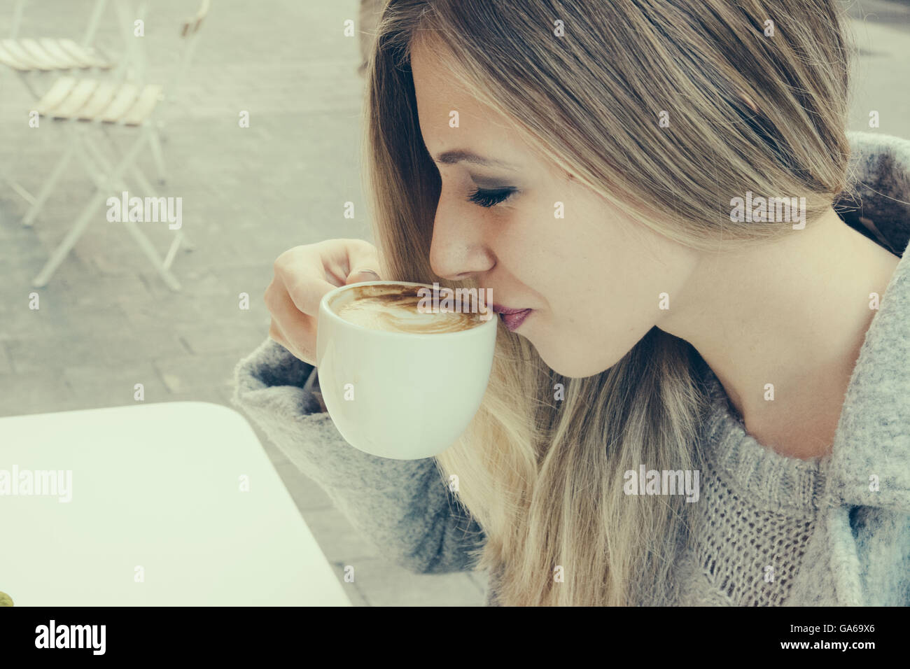Side view of young blonde woman drinking latte while sitting outdoors in cafe Stock Photo