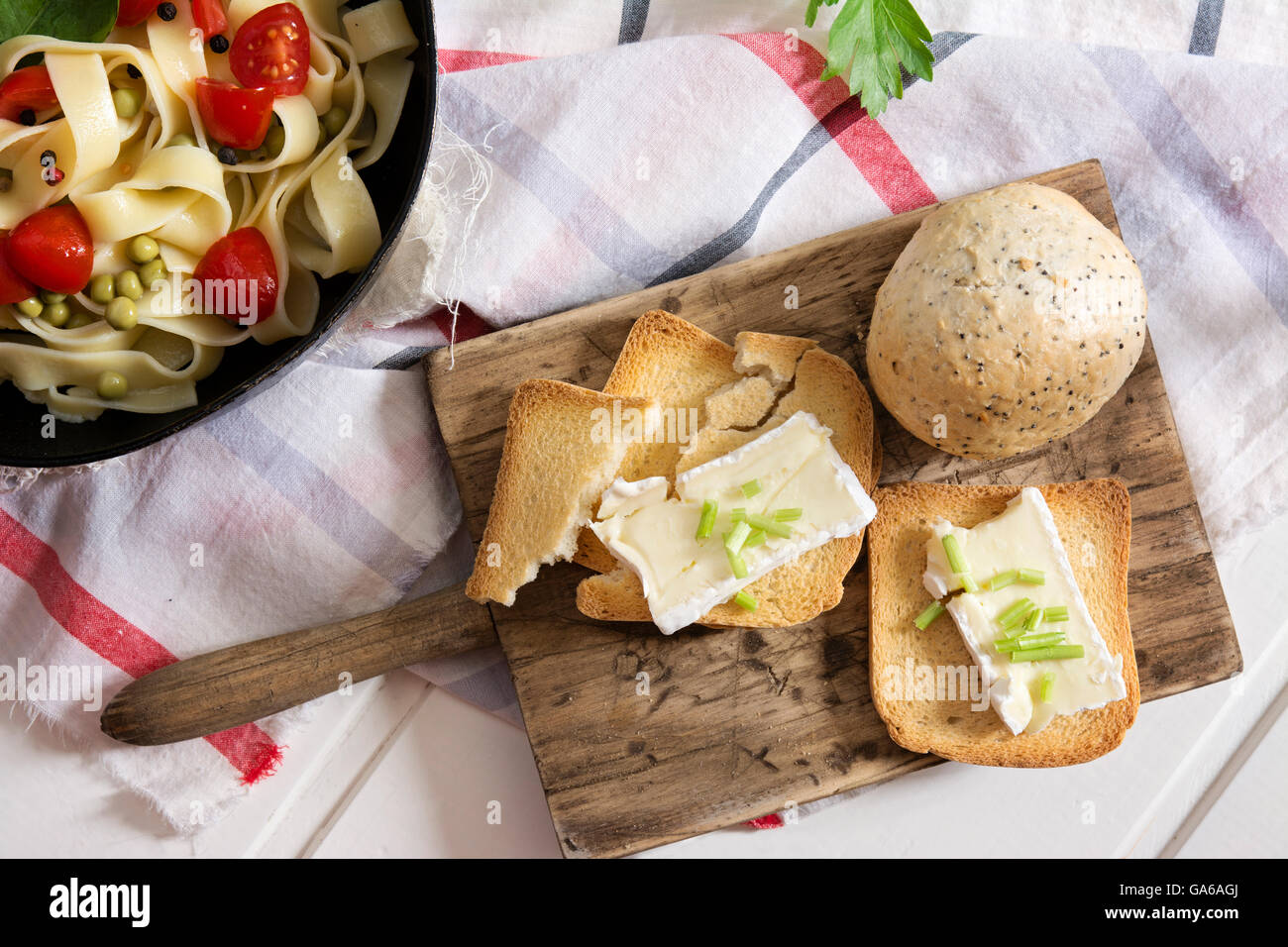 toasted bread, with brie cheese and chives and tagliatelle with cherry tomatoes on checkered tablecloth Stock Photo