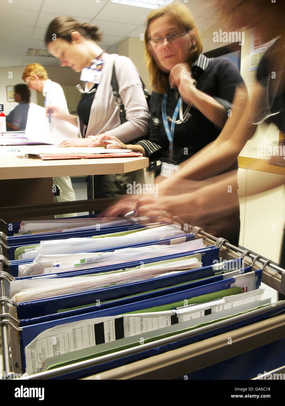 Patient notes with medical staff walking in background and doctors browsing medical files on busy ward in large general hospital Stock Photo