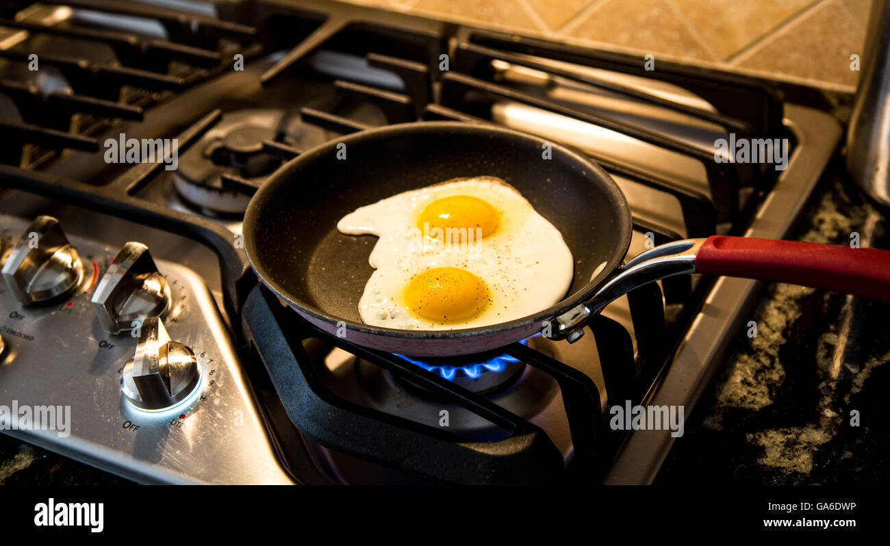Two eggs being fried in a non-stick skillet on a gas range. Stock Photo