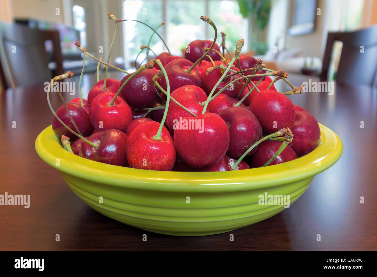 Pile of Bing Cherries in green bowl and on wood dining table Stock Photo