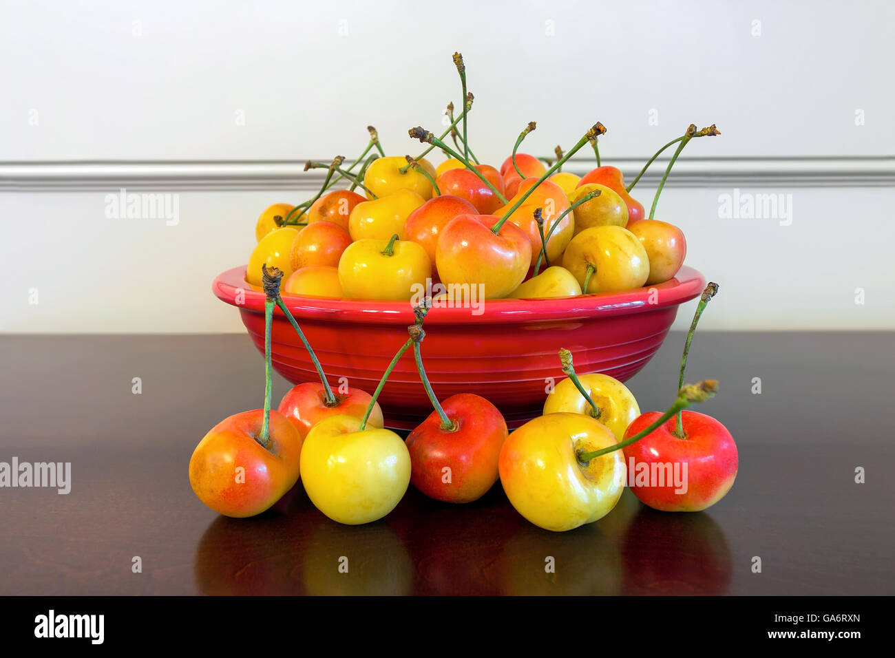 Pile of Rainier Cherries in a red bowl and on a wooden table closeup Stock Photo