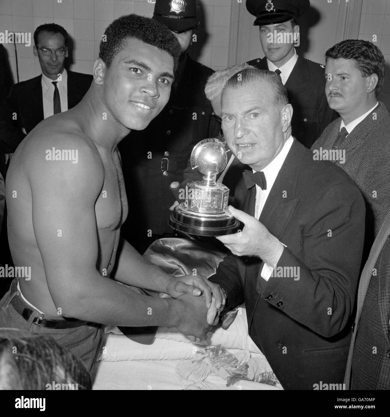 World heavyweight champion Muhammad Ali (Cassius Clay) receiving a trophy from British Boxing Board of Control Secretary Teddy Waltham in his dressing room after retaining his world title by beating Henry Cooper. The referee stopped the fight at the Arsenal Stadium, Highbury in the sixth round when blood was streaming from Cooper's eye. Stock Photo