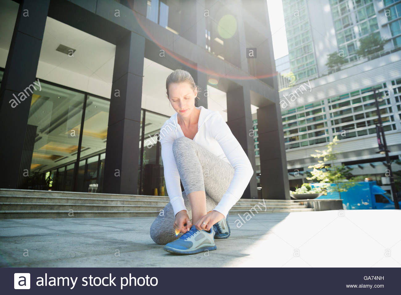 Runner tying shoes on sunny city sidewalk Stock Photo Alamy