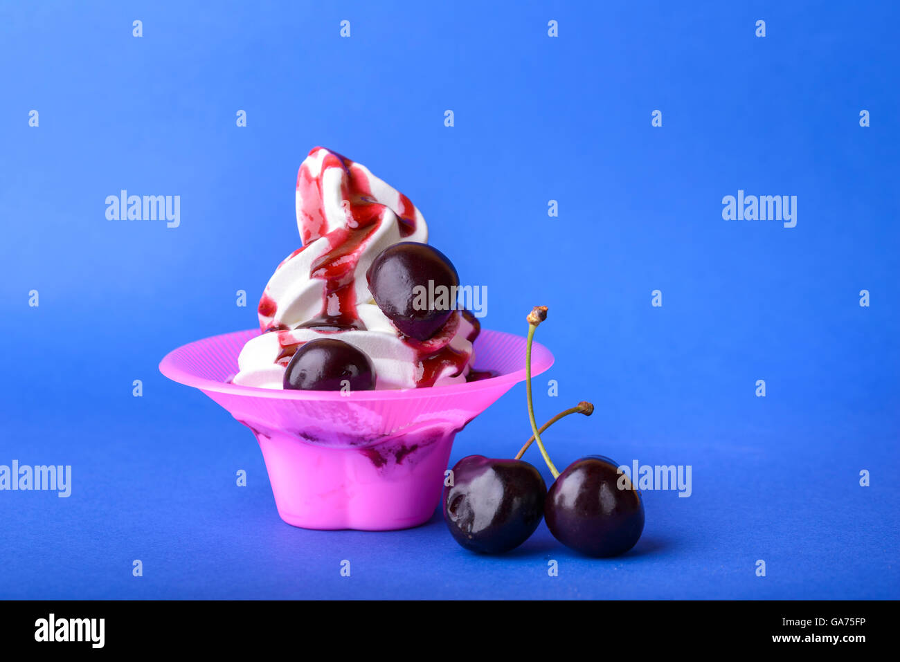 frozen yogurt with black cherry cream and cherry topping on blue background Stock Photo