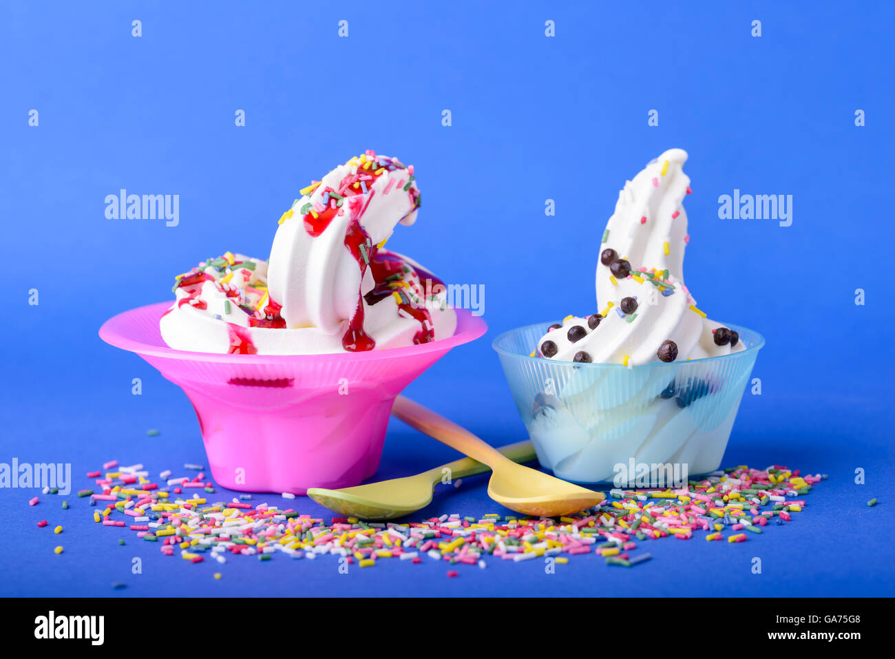 two frozen yogurt with black cherry topping and rainbow sprinkles and chocolate candy on blue