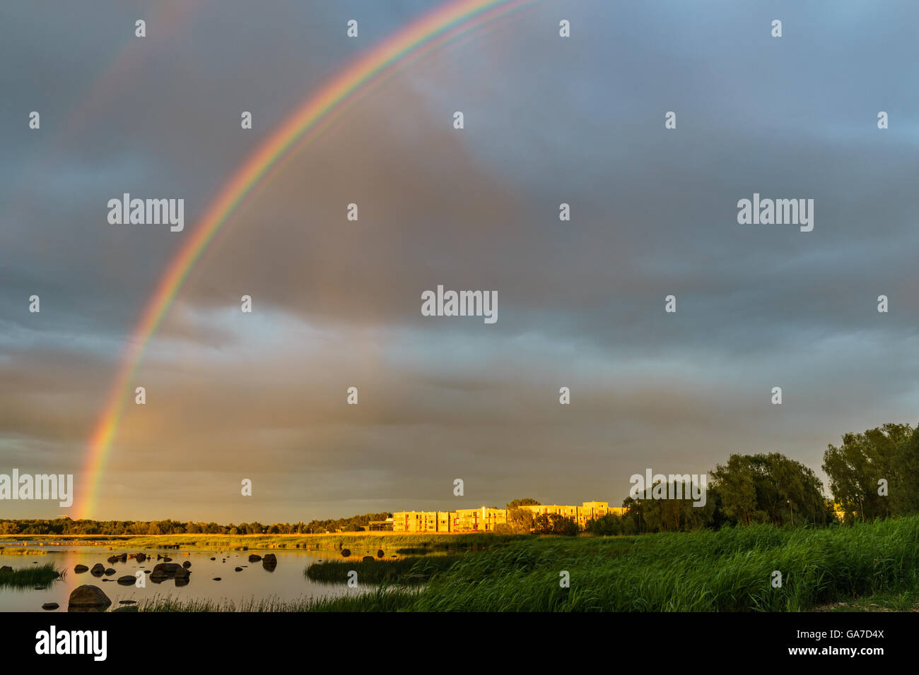 Rainbow over stony seacoast in sunset light. Summertime landscape Stock Photo