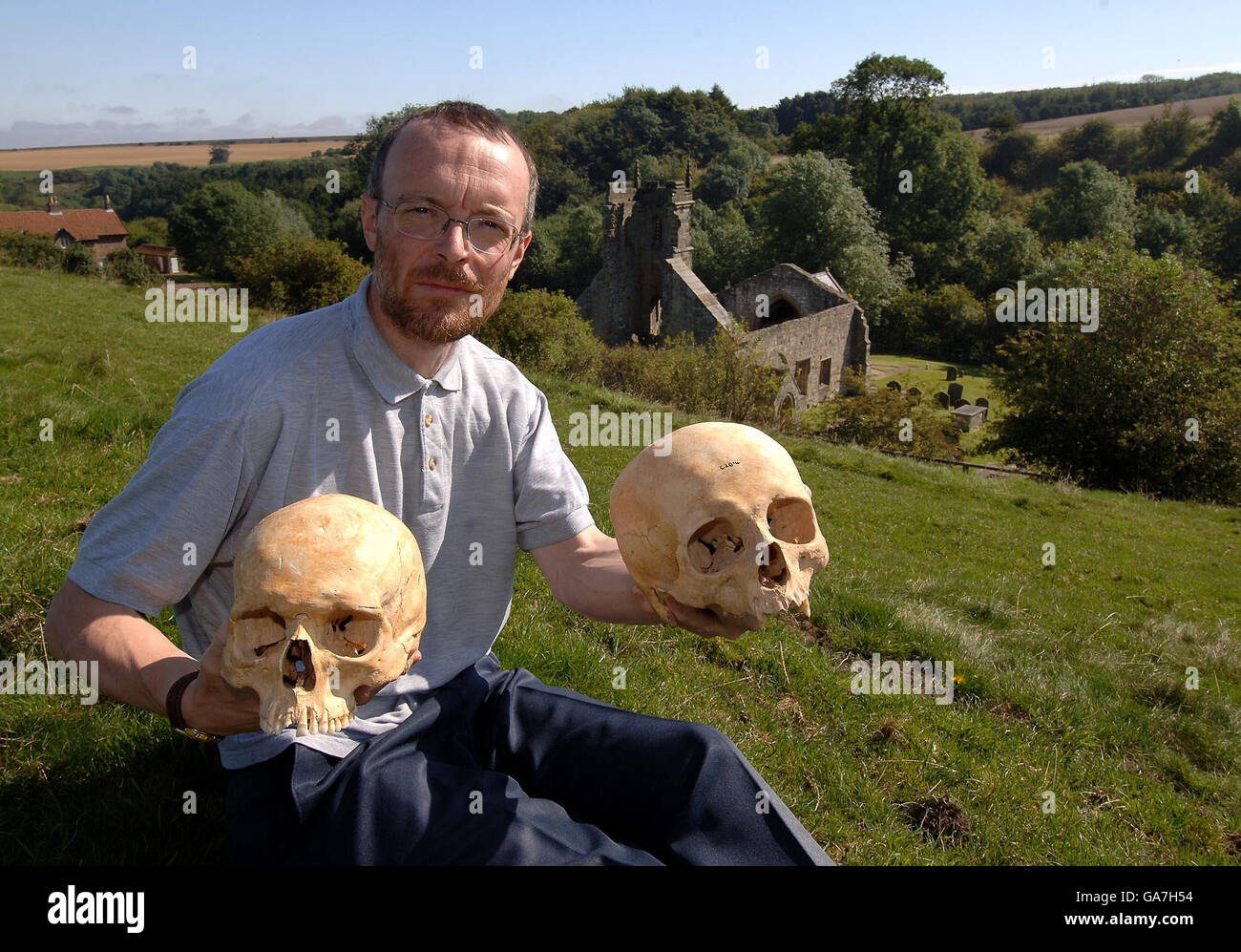 Simon Mays the English Heritage Skeletal Biologist with a 13th Century skull (left) and a 11th Century skull found at the Wharram Percy deserted village (seen in background) that has revealed a puzzling shift in skull shapes of humans between those centuries. Stock Photo