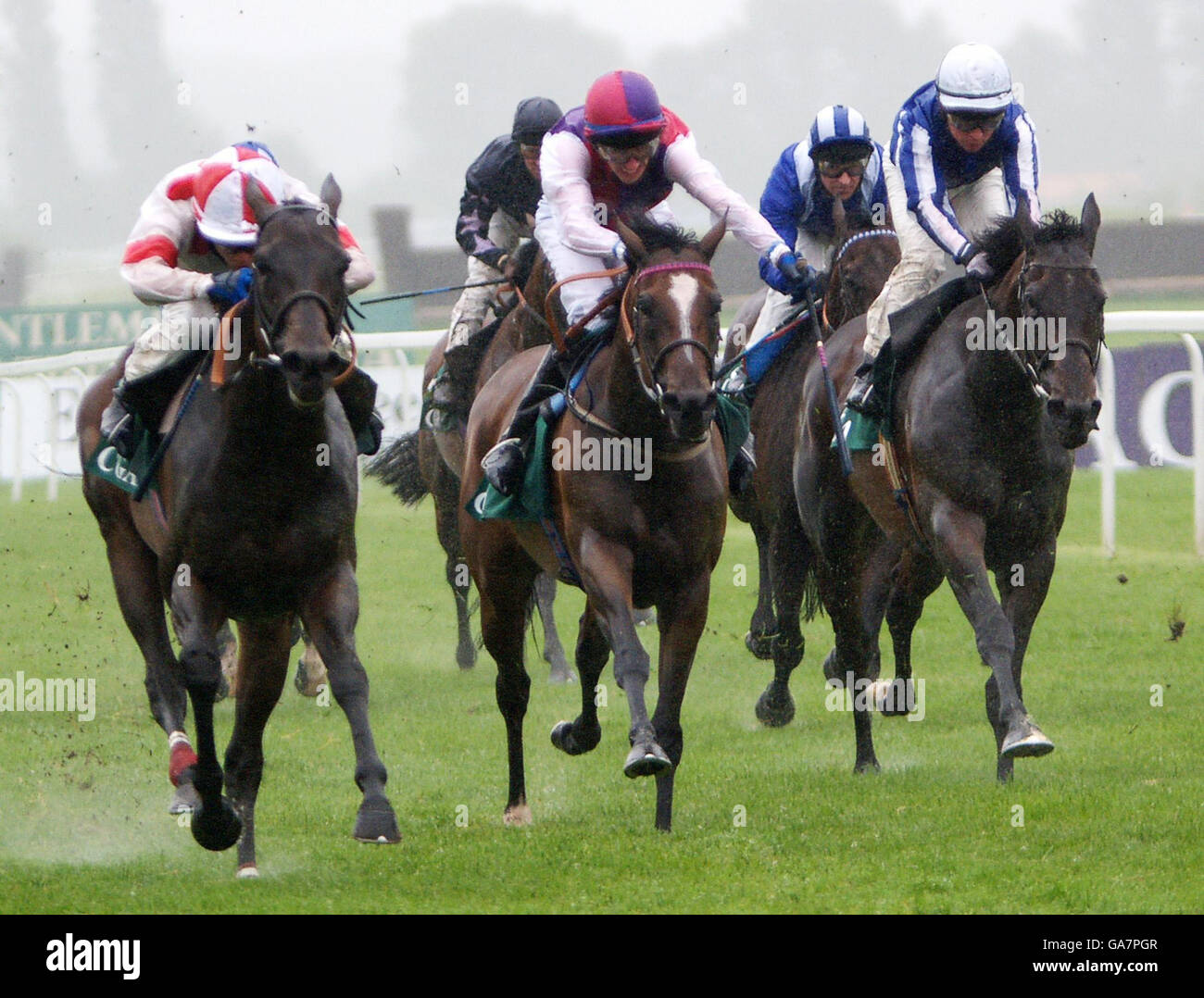 Jamie Spencer takes Red Evie (left) through the driving rain past George Baker, on Wake Up Maggie (centre) and Tadgh O'Shea on Silver Touch (right) to win the CGA Hungerford Stakes at Newbury Racecourse. Stock Photo