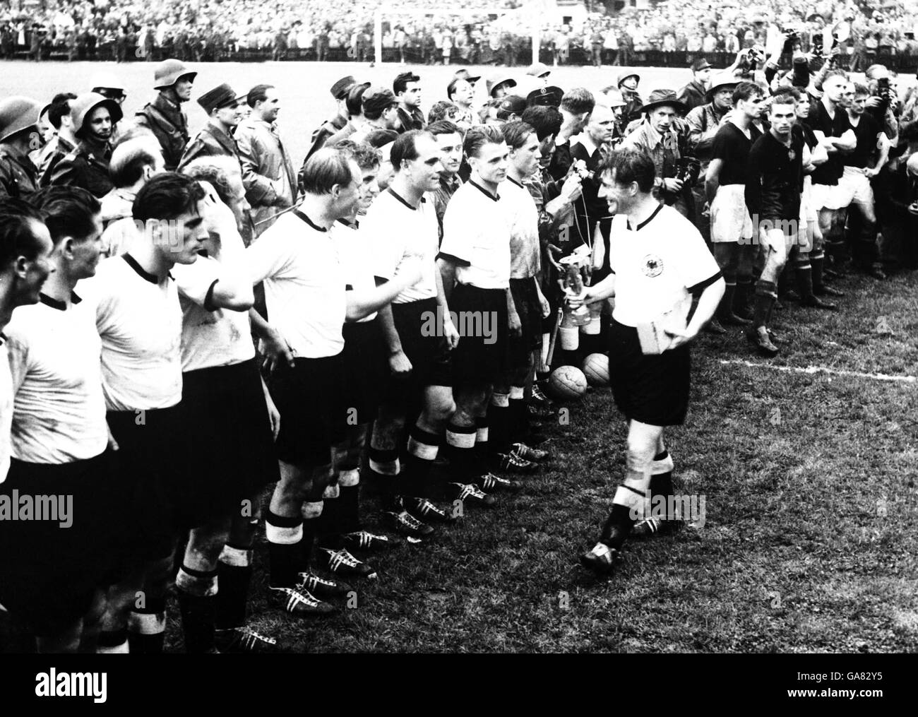 (L-R) West Germany's Horst Eckel, Helmut Rahn, Ottmar Walter, Werner Liebrich, Josef Posipal, Hans Schafer, Werner Kohlmeyer, Karl Mai and Max Morlock watch as grinning captain Fritz Walter returns to the line after collecting the Jules Rimet Trophy following his team's 3-2 victory over Hungary, who look on disappointedly Stock Photo