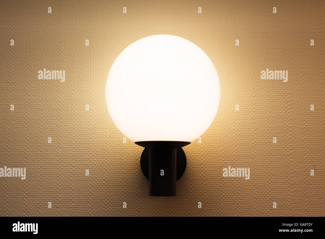 Round wall lamp illuminated white wall with textured wallpaper Stock Photo