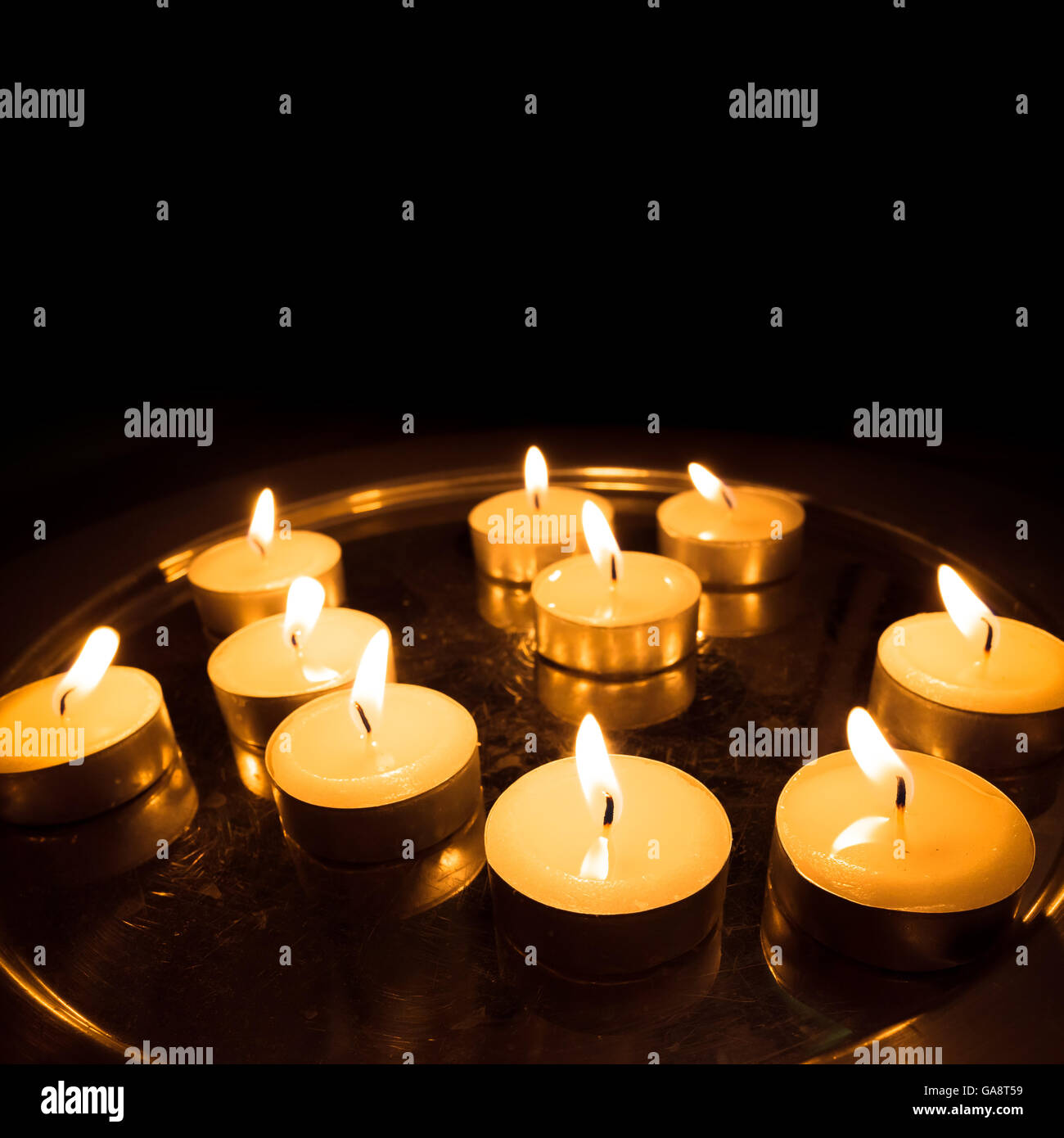 Pray candles burn on a metal stand in the church square photo with black copy-space on upper part Stock Photo
