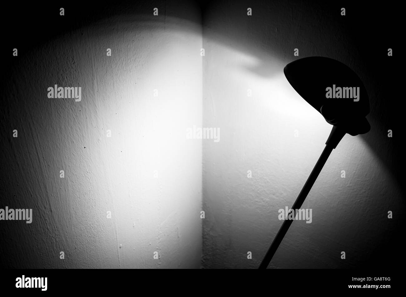 Black reading lamp illuminates the corner of the room painted in white. Spot light and shadows Stock Photo