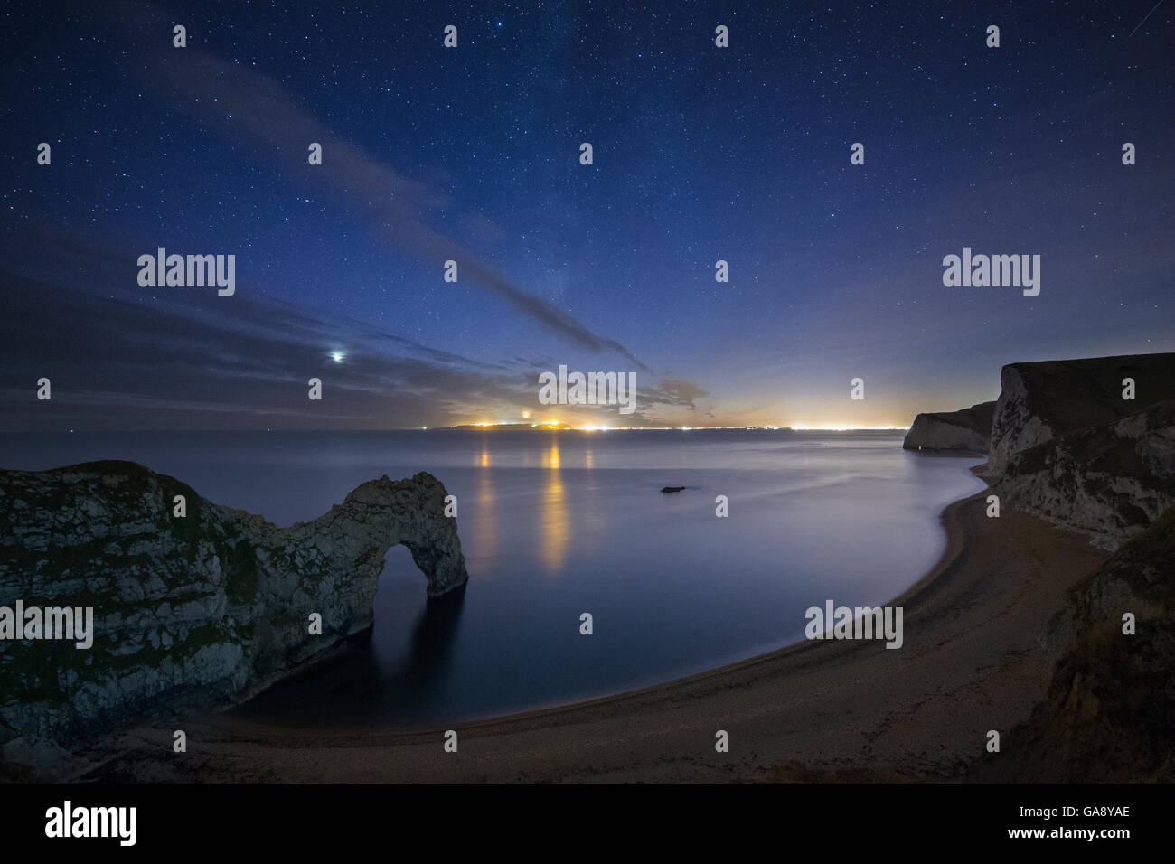 Stars and Milky Way over Durdle Door and the Jurassic Coast, with the lights of Weymouth and Portland beyond, Dorset, England, UK, December 2013. Stock Photo