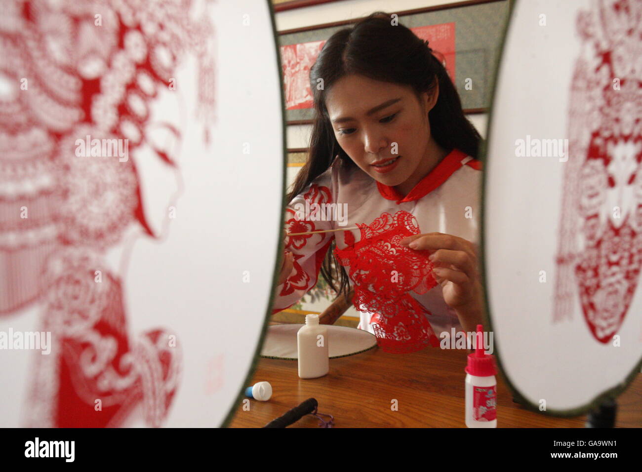 (160804) -- YANTAI, Aug. 4, 2016 (Xinhua) -- Liang Qiaoyan, a paper cutting folk artist, works on her paper cuttings on fans at a studio in Yantai, east China's Shandong Province, Aug. 3. 2016. Liang has made over 40 kinds of handiworks of paper cutting as she combined the cutting with porcelain, statue, cloth and etc. (Xinhua/Shen Jizhong) (wyl) Stock Photo
