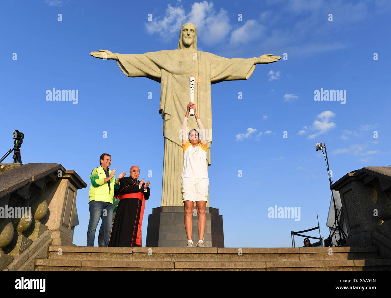 Rio de Janeiro, Brazil. 5th Aug, 2016. Brazilian former volleyball player Maria Isabel Barroso holds the Olympic torch next to Eduardo Paes (L), Mayor of Rio de Janeiro, and Archbishop of Rio de Janeiro, Orani Joao Tempesta (2-L), during the Olympic Torch Relay in front of Christ the Redeemer statue early in the morning prior to the Rio 2016 Olympic Games in Rio de Janeiro, Brazil, 5 August 2016. Rio 2016 Olympic Games take place from 05 to 21 August. Photo: Sebastian Kahnert/dpa/Alamy Live News Stock Photo