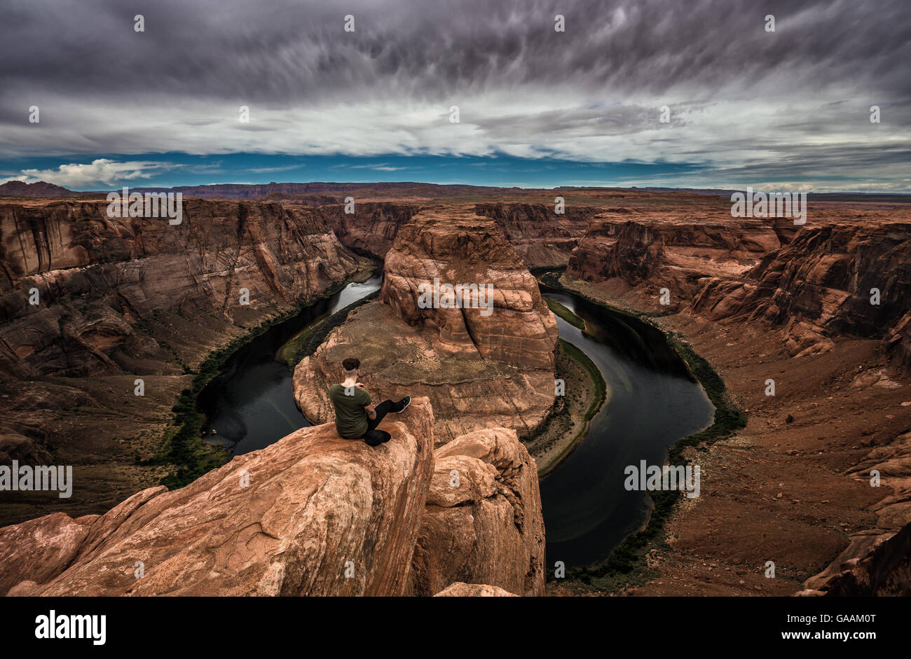 Horseshoe Bend, Colorado river and a hiker sitting at the edge and enjoying the panoramic view. Stock Photo