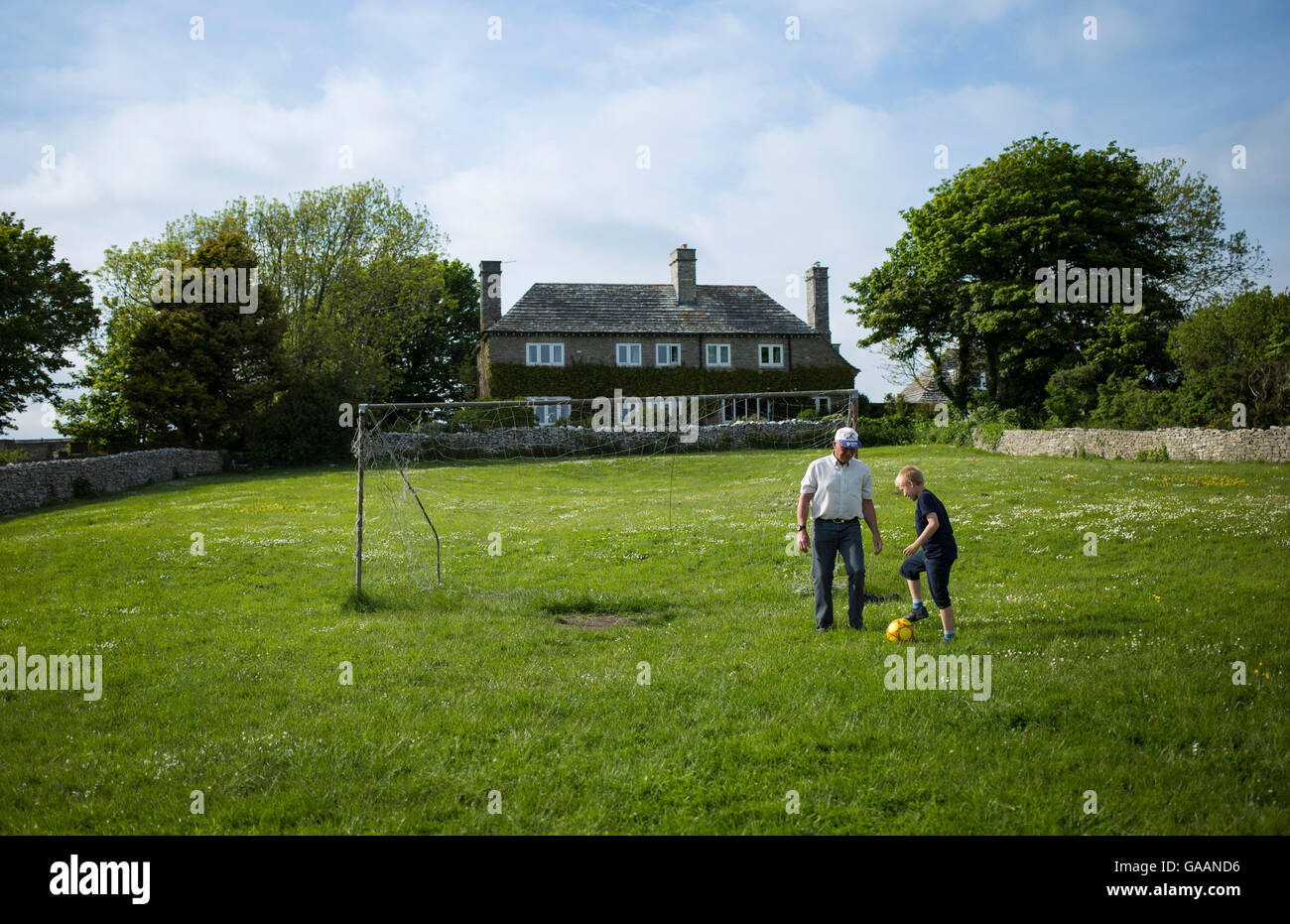 A young boy and an older man play football in a field outside Worth Matravers, Dorset, UK Stock Photo