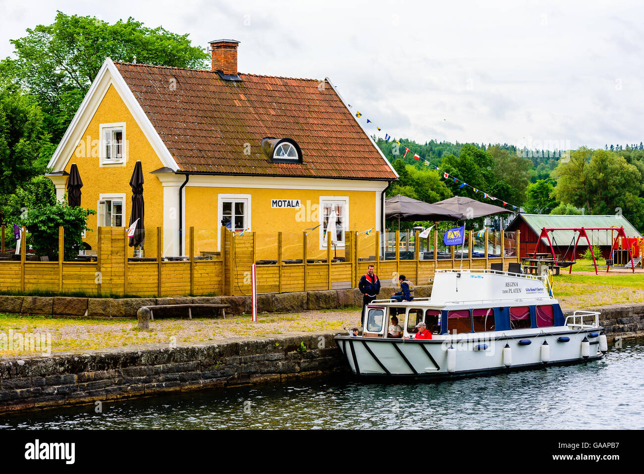 Motala, Sweden - June 21, 2016: Small yellow house with the text Motala on the facade. Chartered boat moored outside in the cana Stock Photo