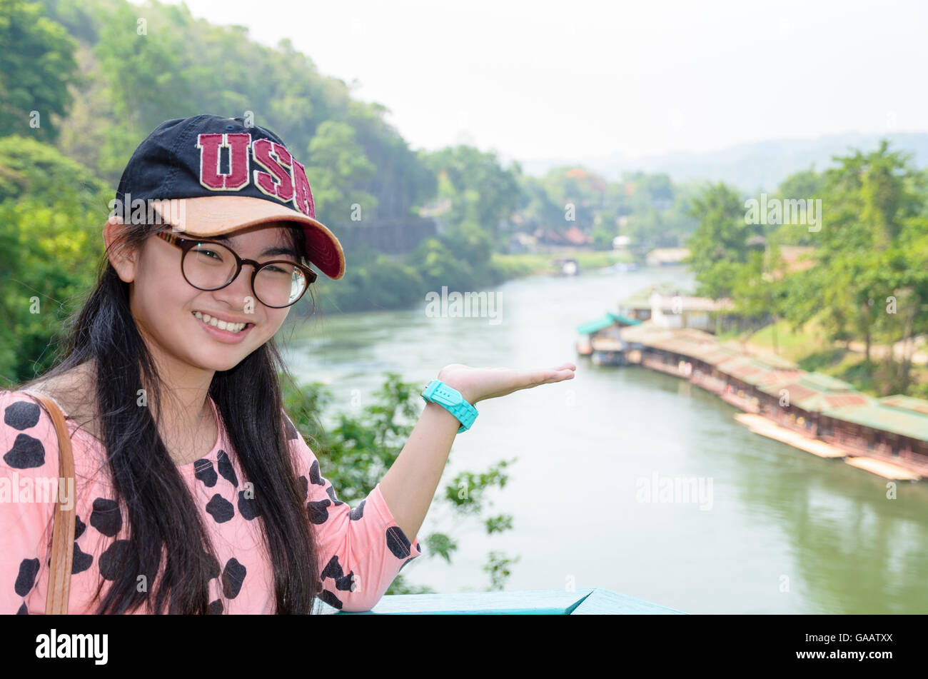 Tourist girl show hands invites to visit beautiful landscape of Death Railway bridge over the Kwai Noi River at Krasae cave view Stock Photo
