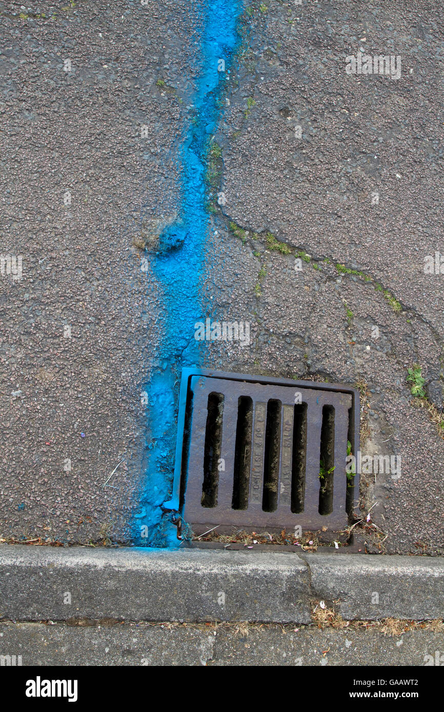 Blue line sprayed on to road surface by a drain as a road race start line Stock Photo