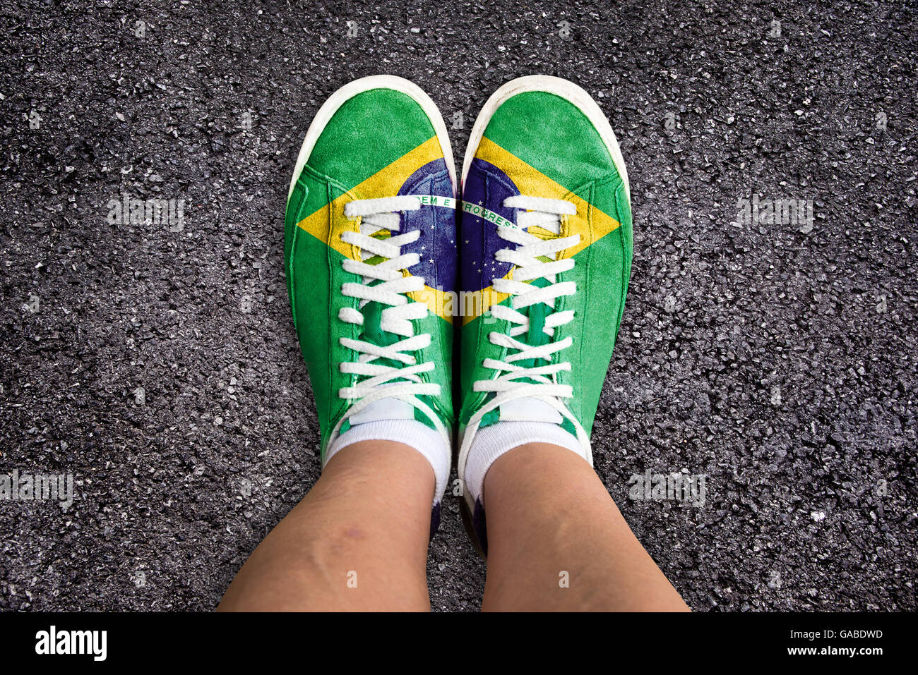 Legs wth sport shoes colored the brazilian flag, asphalt background Stock Photo