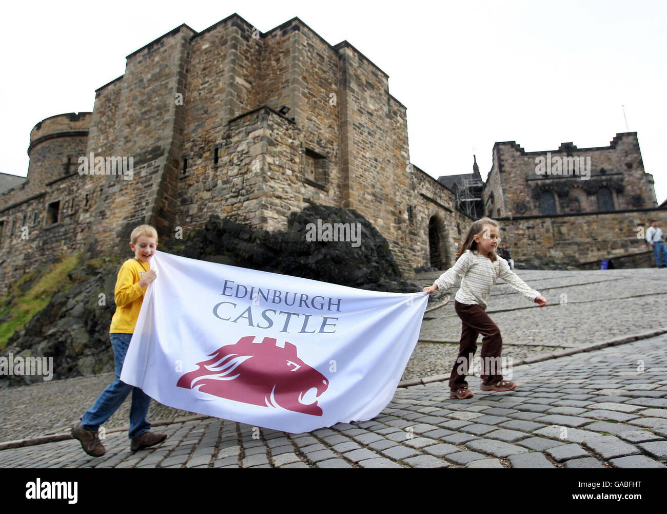 Visitors Will and Laura Sutherland at Edinburgh Castle running with a flag bearing the new logo for the landmark, launched at the castle today which is perched on a 340 million year old volcano in the city centre. Stock Photo