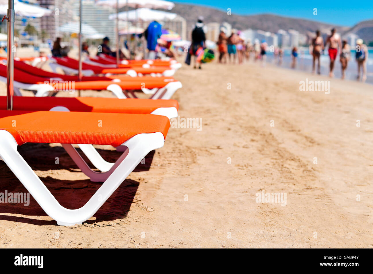 closeup of some sunloungers and umbrellas in San Antonio Beach in Cullera, Spain, with the Mediterranean sea and some unrecogni Stock Photo