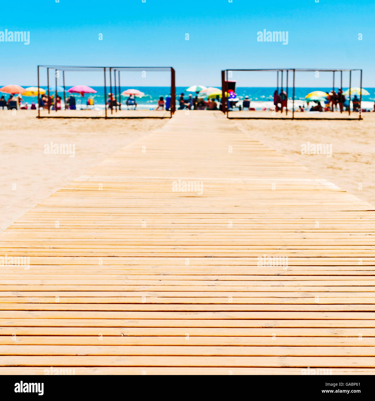 wooden boardwalk at the San Antonio Beach in Cullera, Spain, with the Mediterranean sea and unrecognizable sunbathers in the bac Stock Photo