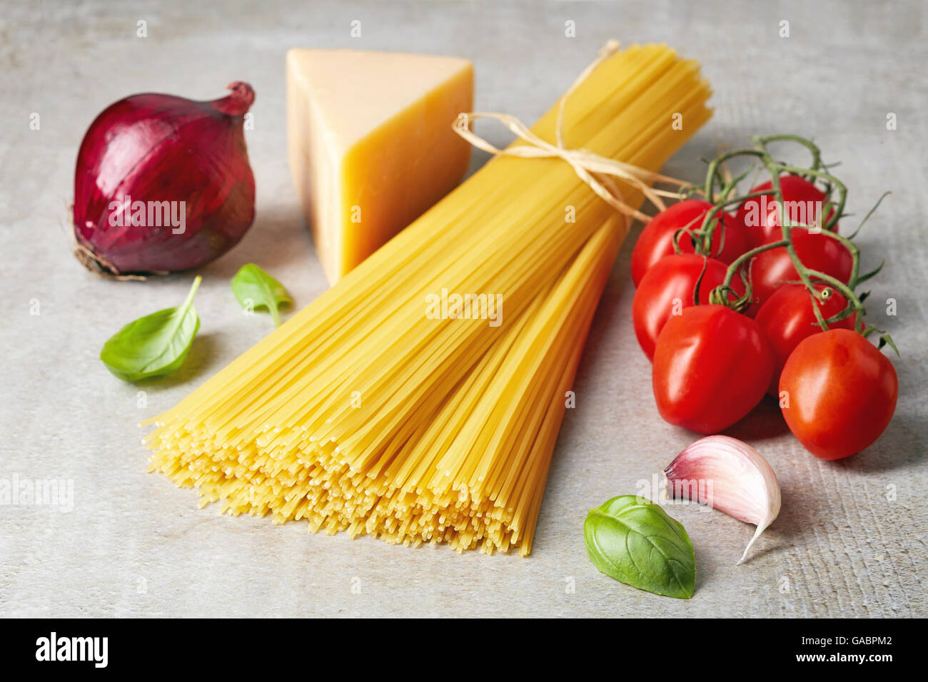 Spaghetti pasta, tomato, cheese, onion, garlic and basil leaves on grey stone table Stock Photo