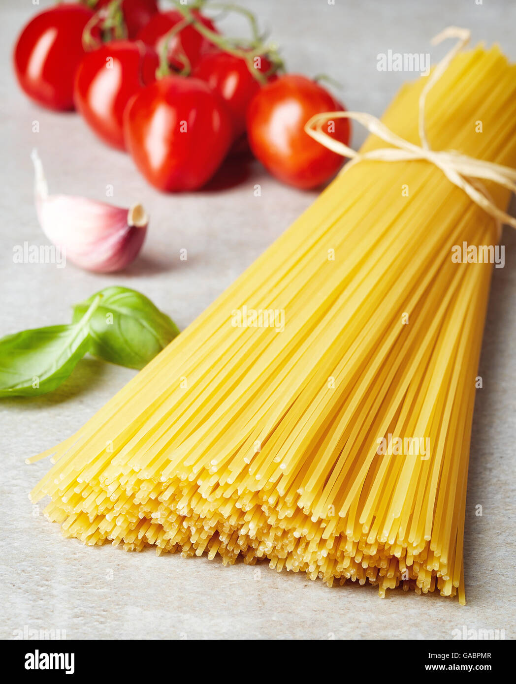 Spaghetti pasta, tomato, garlic and basil leaves on grey stone table Stock Photo