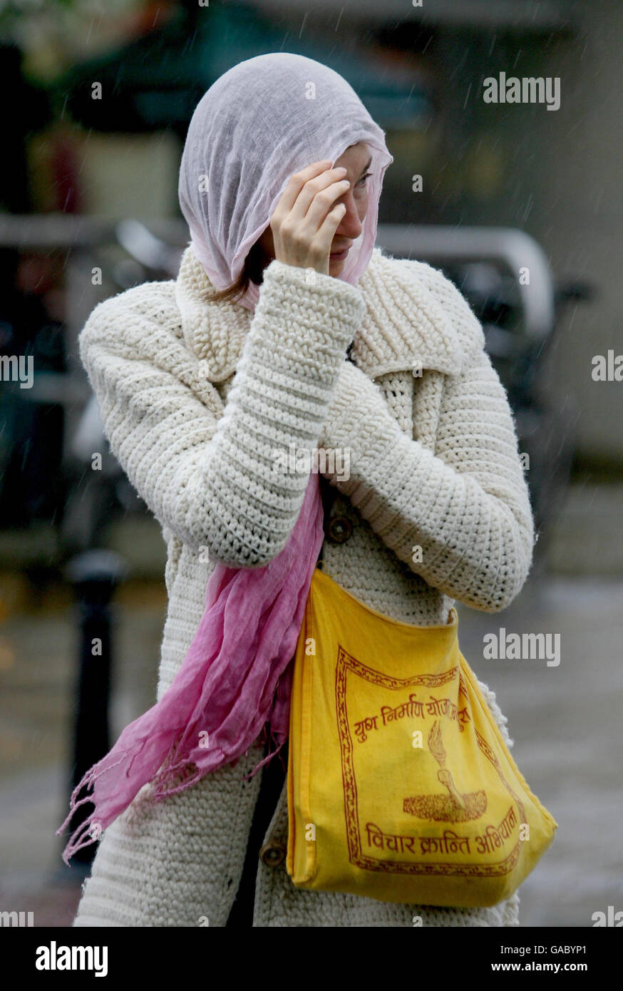 A woman covers her head with a scarf as heavy rain hits Bristol Stock
