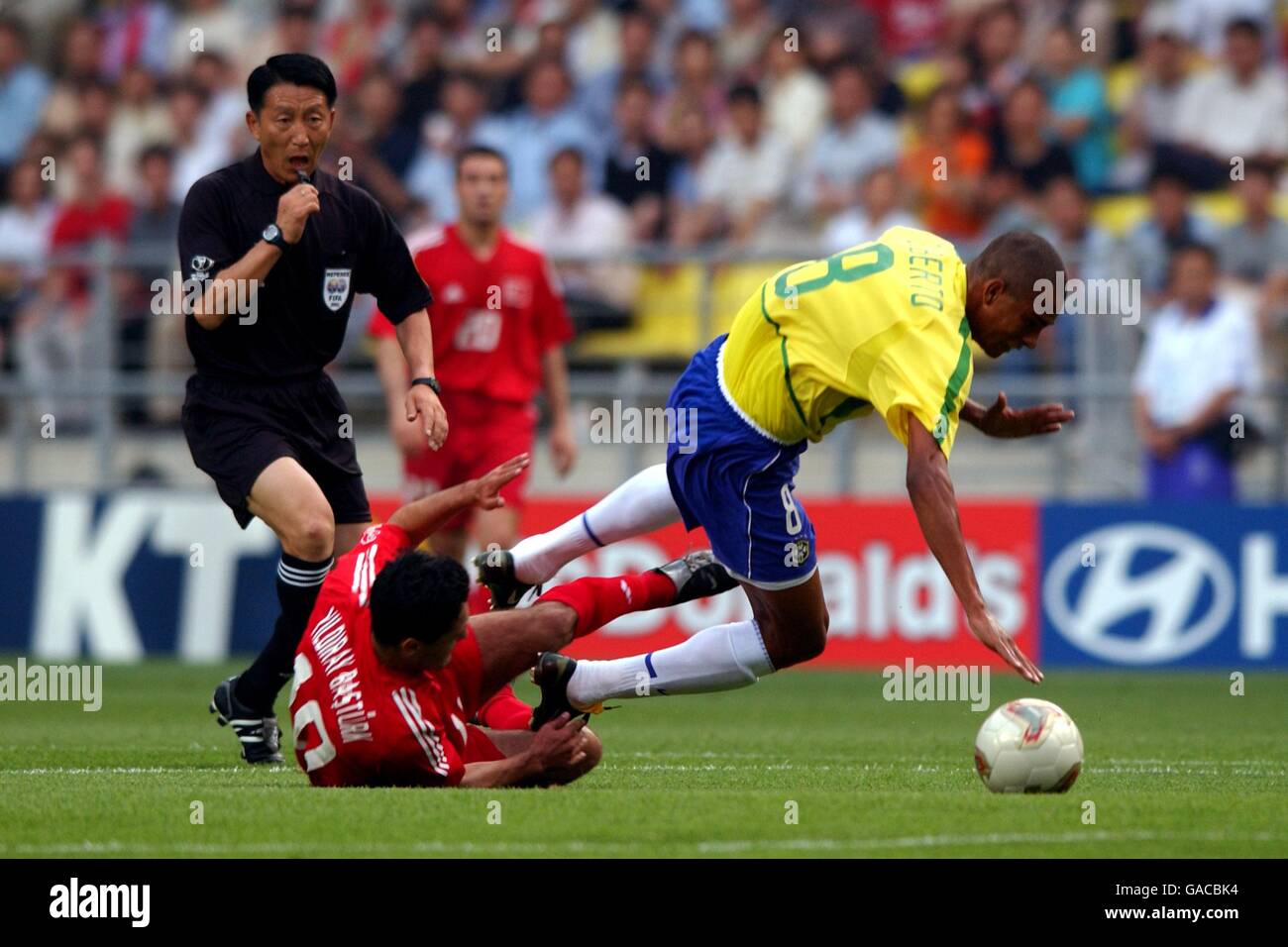 Soccer - FIFA World Cup 2002 - Group C - Brazil v Turkey. Turkey's Yildiray Basturk (c) brings down Brazil's Gilberto Silva (r) under the nose of Referee Young Joo Kim (l) Stock Photo