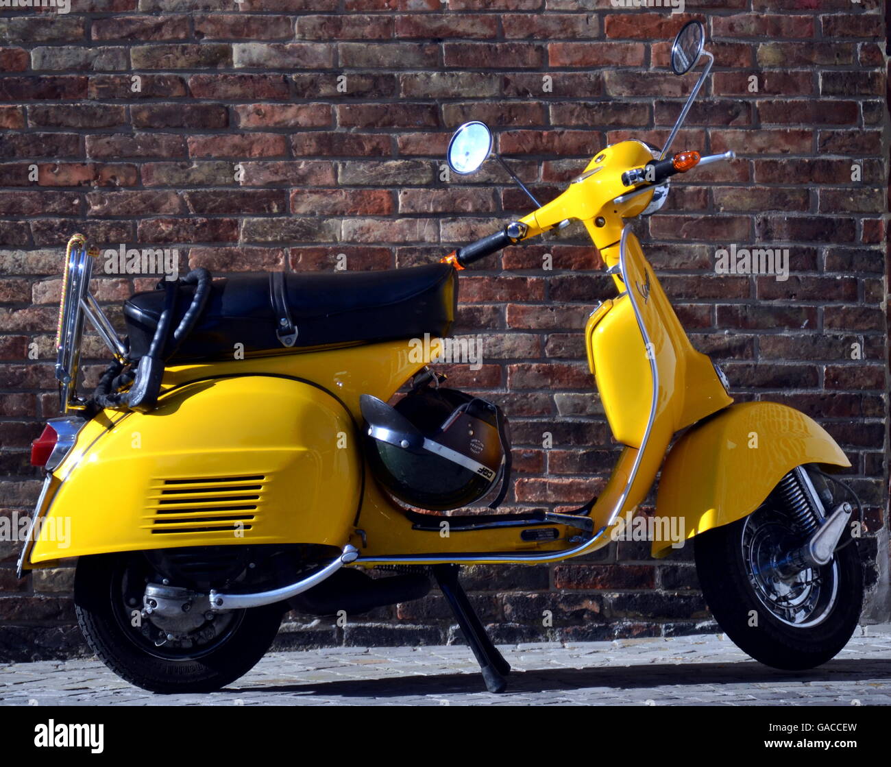 Vespa -Yellow Vespa scooter parked against brick wall Stock Photo