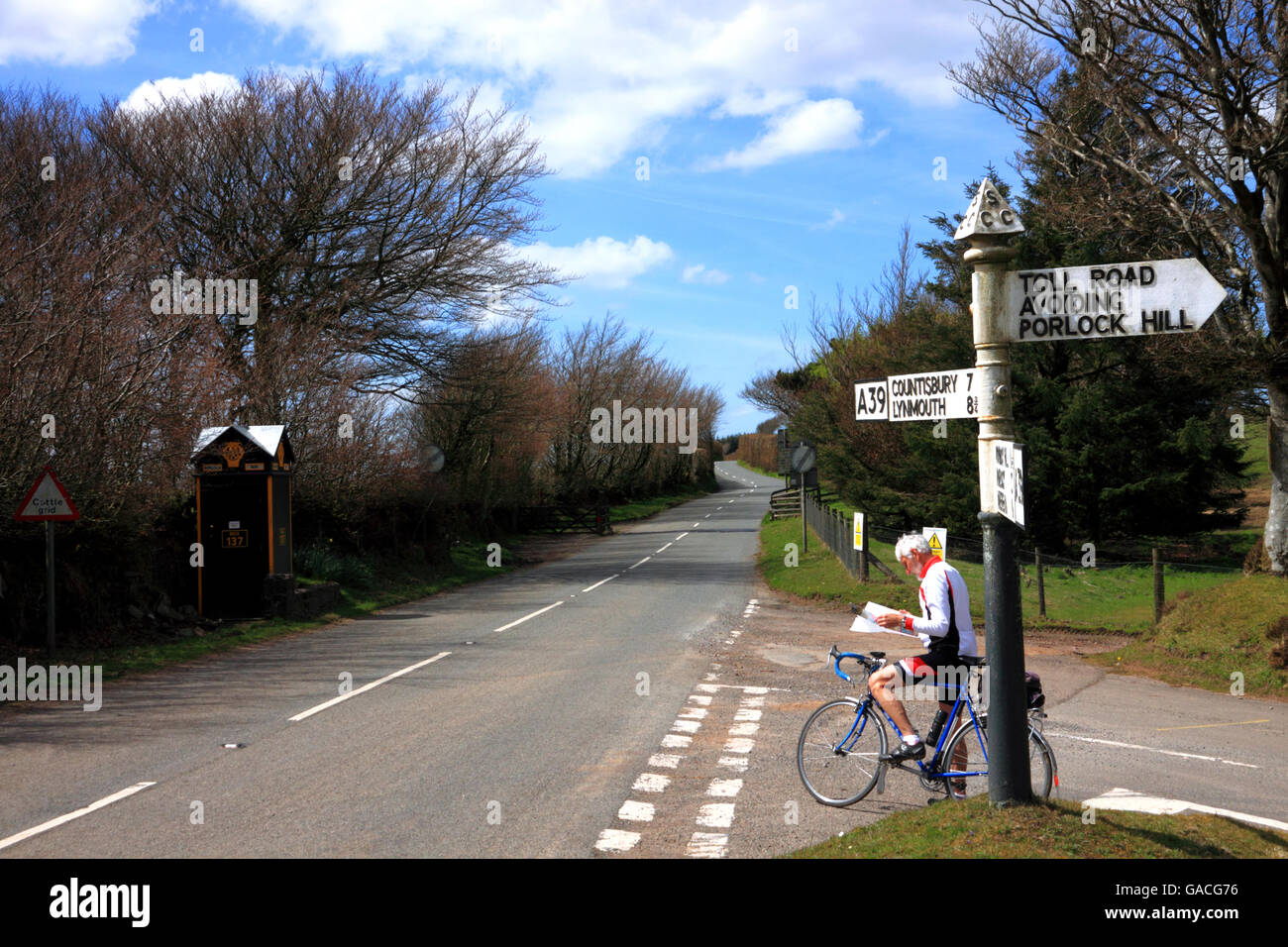 A cyclist consulting his map at a crossroads with a signpost destination Countisbury and Lynmouth, Toll Road avoiding Porlock. Stock Photo