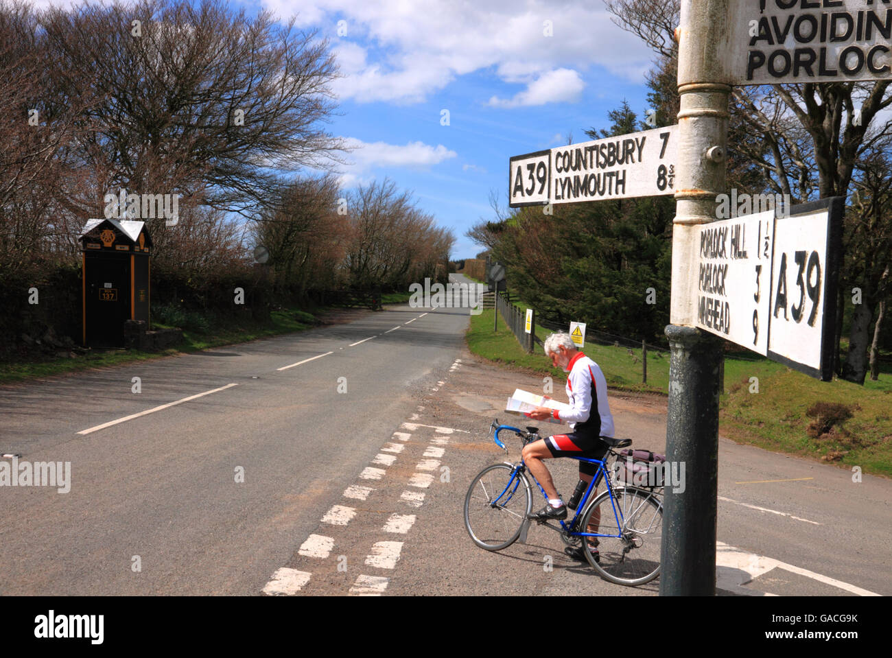 A cyclist consulting his map at a crossroads with a signpost ...