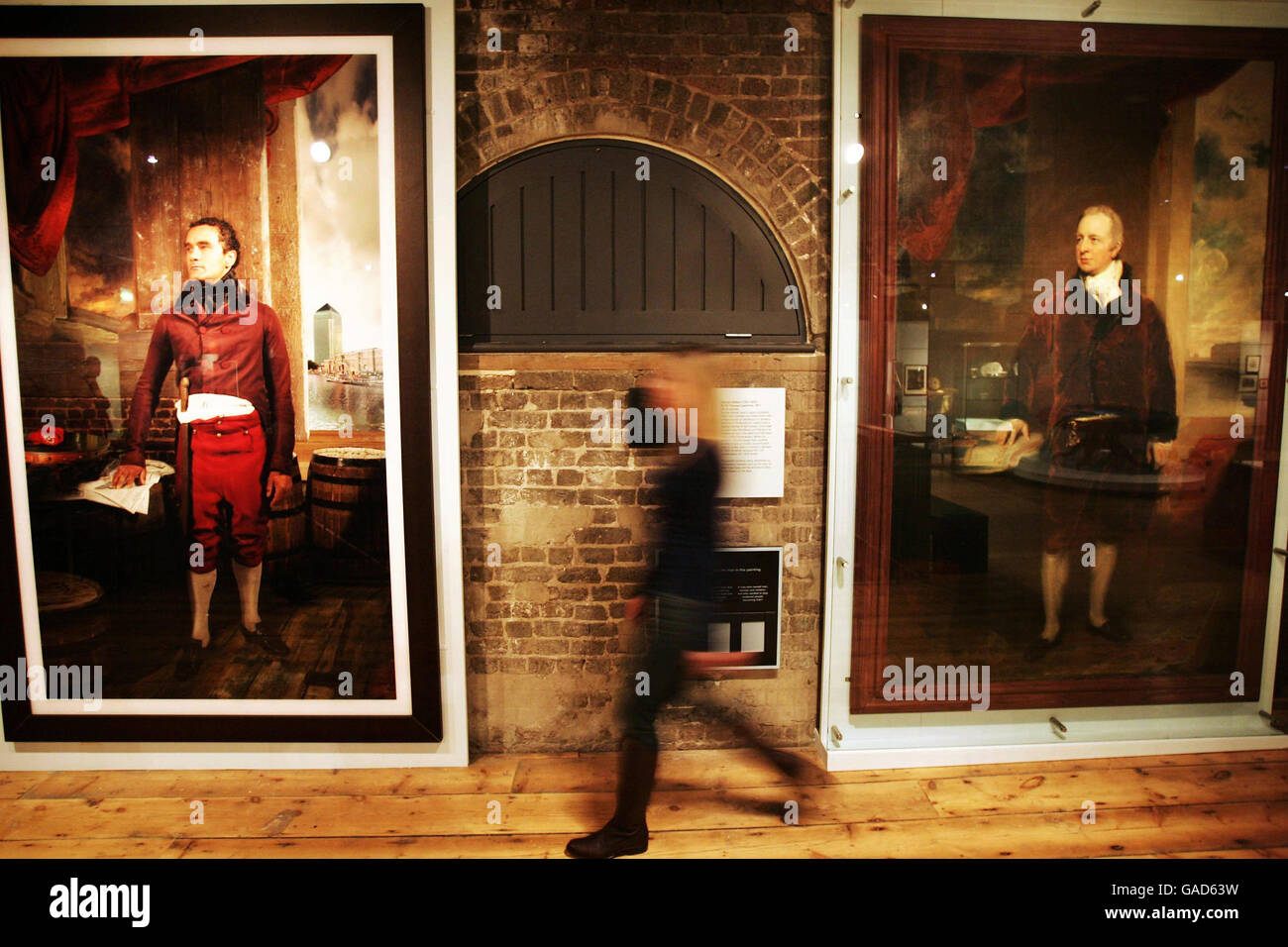 A member of staff walks between portraits of slave trader George Hibbert (right) and a modern reconstructed laserchrome photograph on aluminium portrait of Lloyd Gordon as Robert Wedderburn, at the 'London, Sugar & Slavery' at The Museum in Docklands, London. Stock Photo