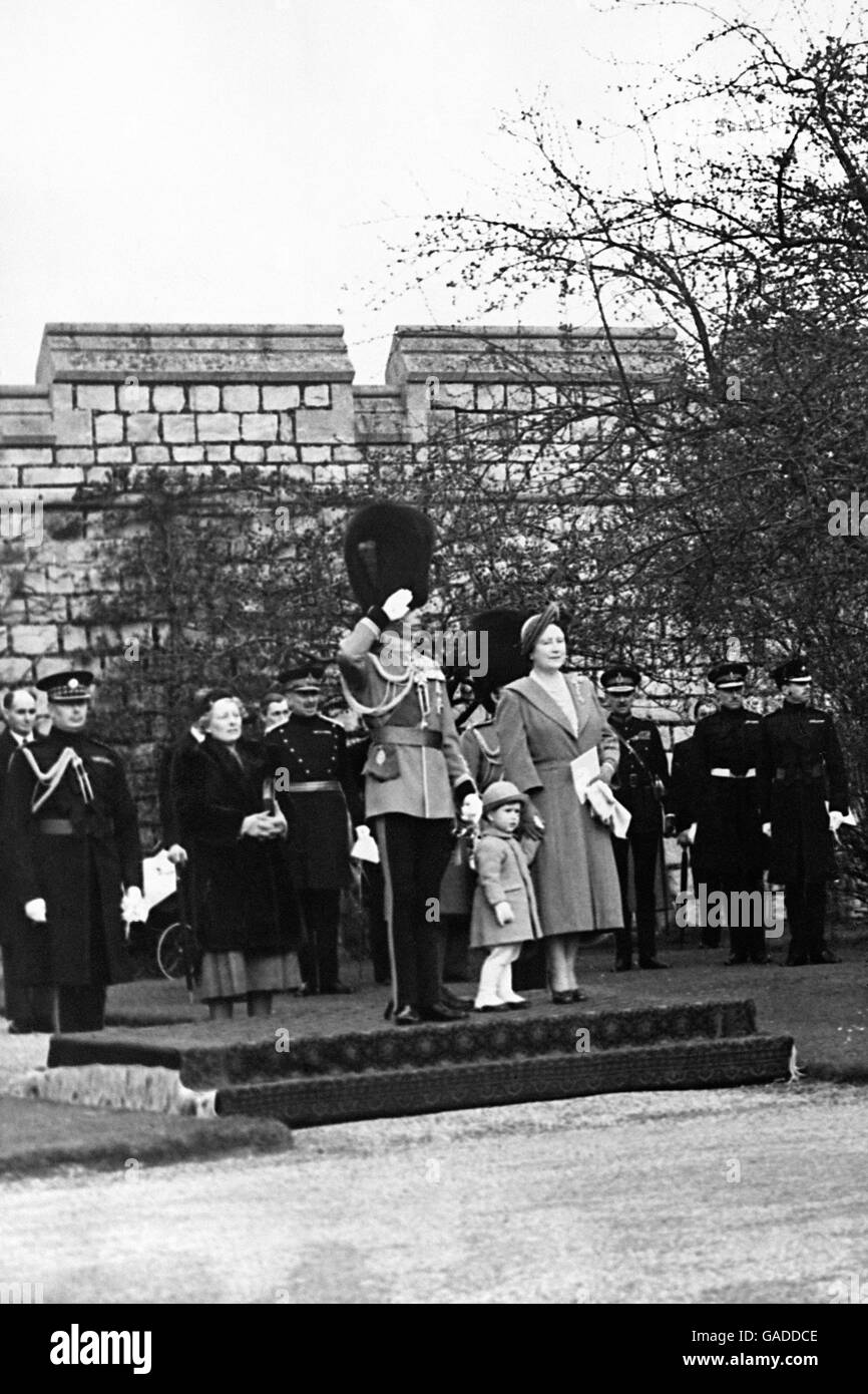 Holding the hand of his Grandmother the Queen, the young Prince Charles stands by the King at the saluting base as the Royal grandfather takes the salute at the march past which followed the presentation by the King of new Colours to the 1st and 2nd Battallion of the Coldstream Guards at Windsor Castle. The ceremony took place on the fairway leading to the ninth hole of the Royal Golf course, since the Quadrangle where such ceremonies usually take place is not large enough to accomadate two battalions on parade. Stock Photo