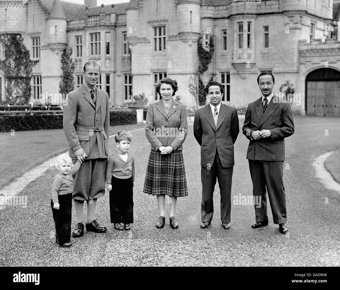 Queen Elizabeth II, wearing a tartan skirt and tweed jacket outside Balmoral Castle with her Royal visitors, King Faisal II and the Regent of Iraq, and the Duke of Edinburgh, Prince Charles and Princess Anne. Stock Photo