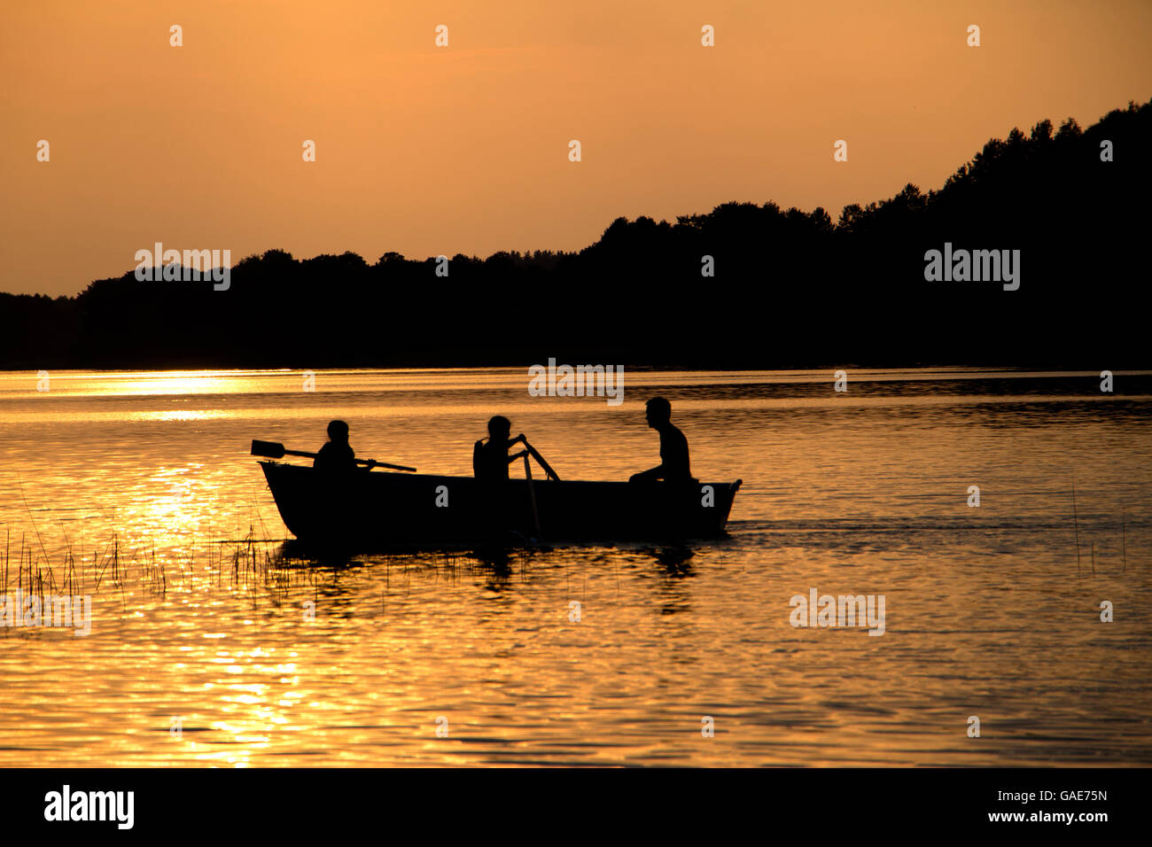 rowing wooden boat on lake in late evening with two girls and father people silhouettes Stock Photo
