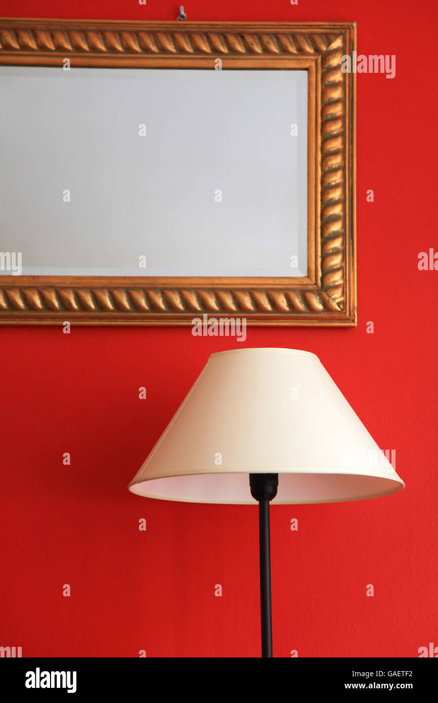 Lamp and framed mirror on red stylish wall Stock Photo