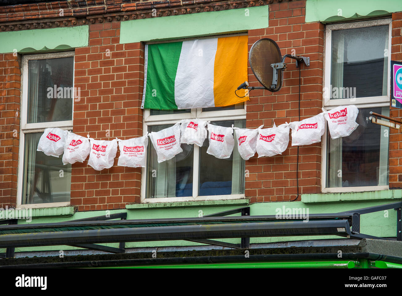 An Irish tricolour flag hangs from a West Belfast flat window along with Iceland shopping bags after Iceland defeated England Stock Photo