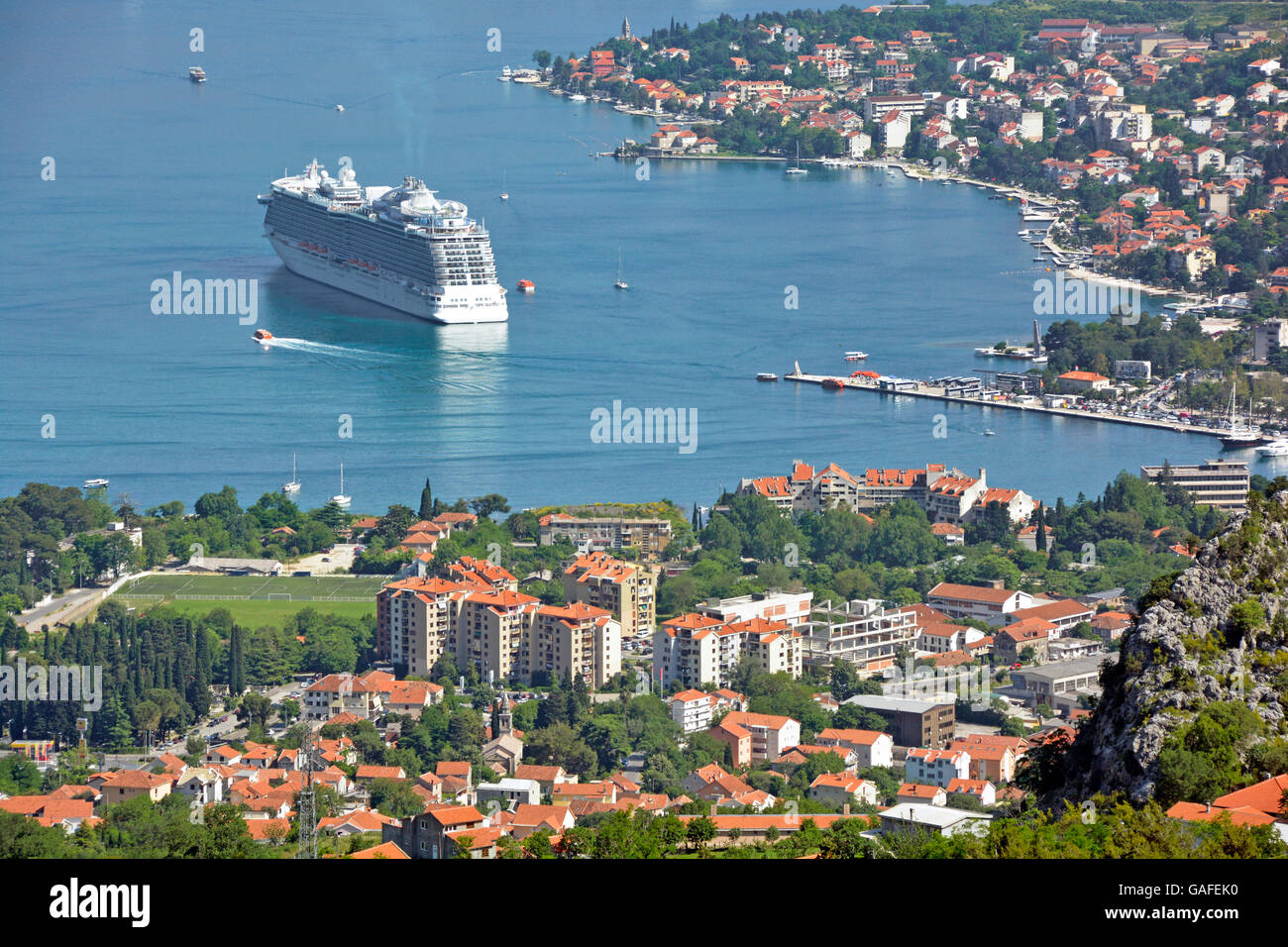 View from above looking down on town & Bay of Kotor Montenegro cruise ship liner Regal Princess using tenders to transport passengers to shallow jetty Stock Photo