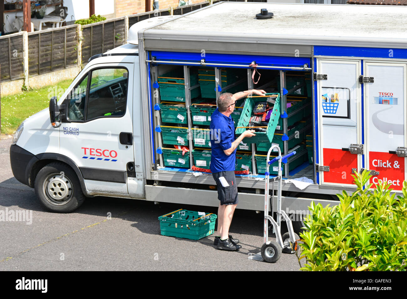 Home delivery van driver at work unloading groceries onto trolley at online customers house from Tesco Supermarket in residential street England UK Stock Photo