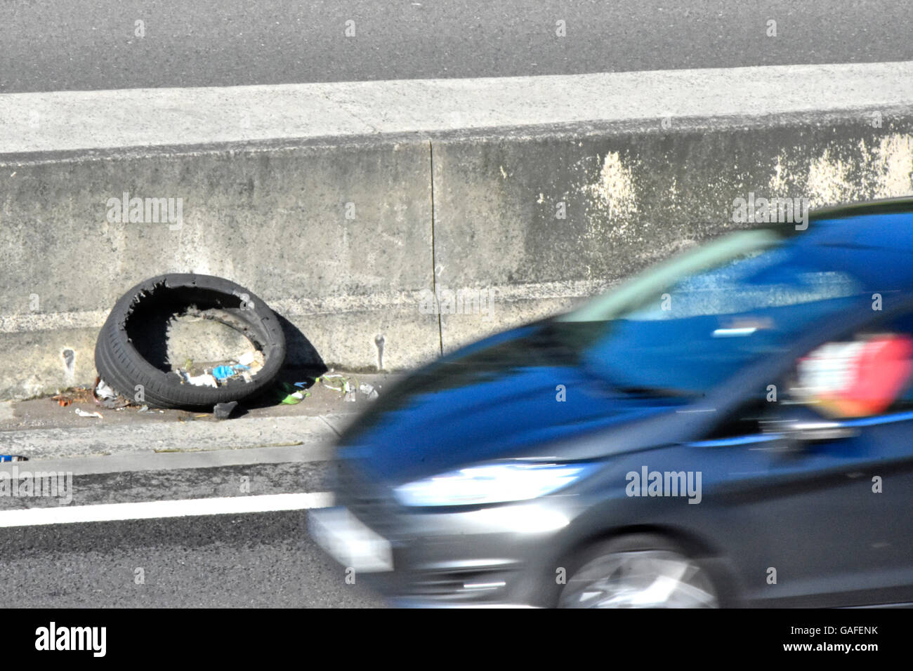 Damaged tyre propped up against central concrete crash barrier beside lane 4 of M25 motorway with fast car passing think concept tyres danger risk Stock Photo