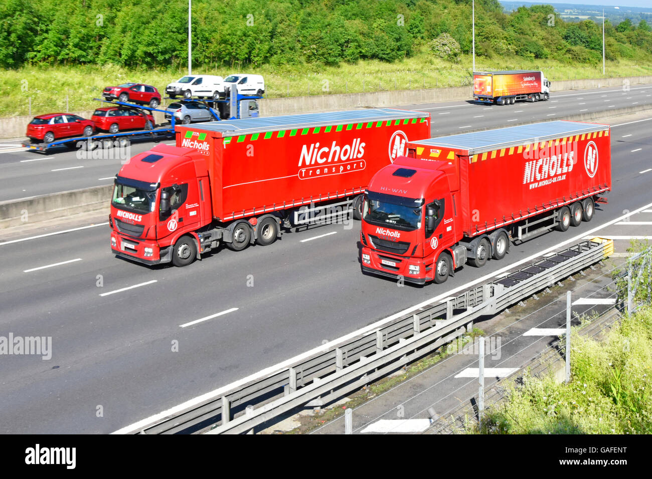 Transportation supply chain logistics via 'Two of a Kind' concept image of two red haulage contractors lorries & trailers on UK four lane UK motorway Stock Photo