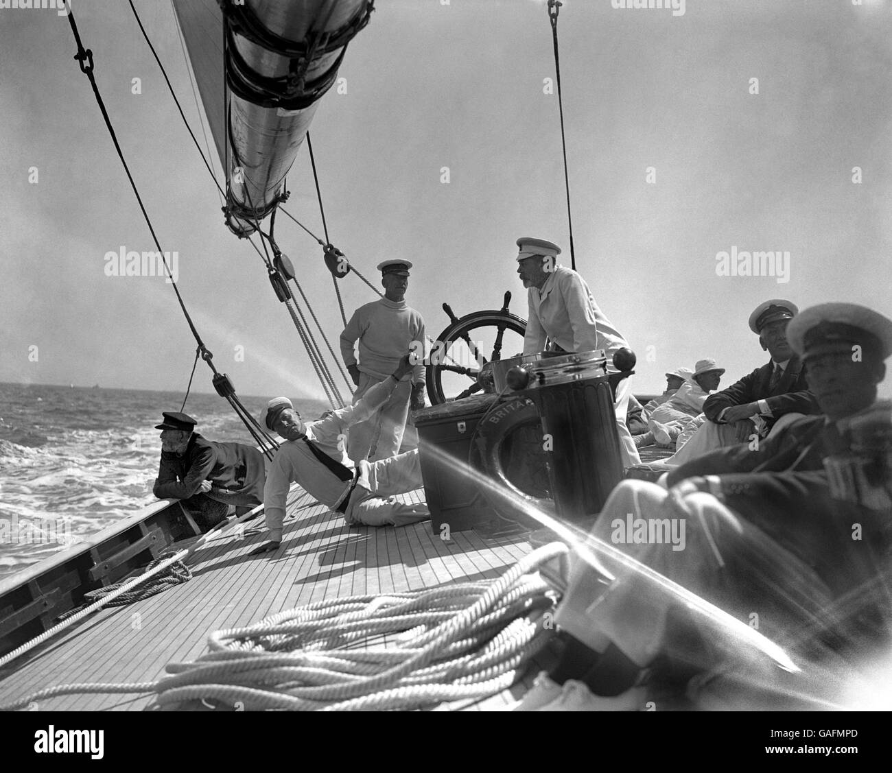 King George V on his yacht 'Britannia' during the racing at Cowes. Major Hunloke, the skipper, is at the wheel. Stock Photo
