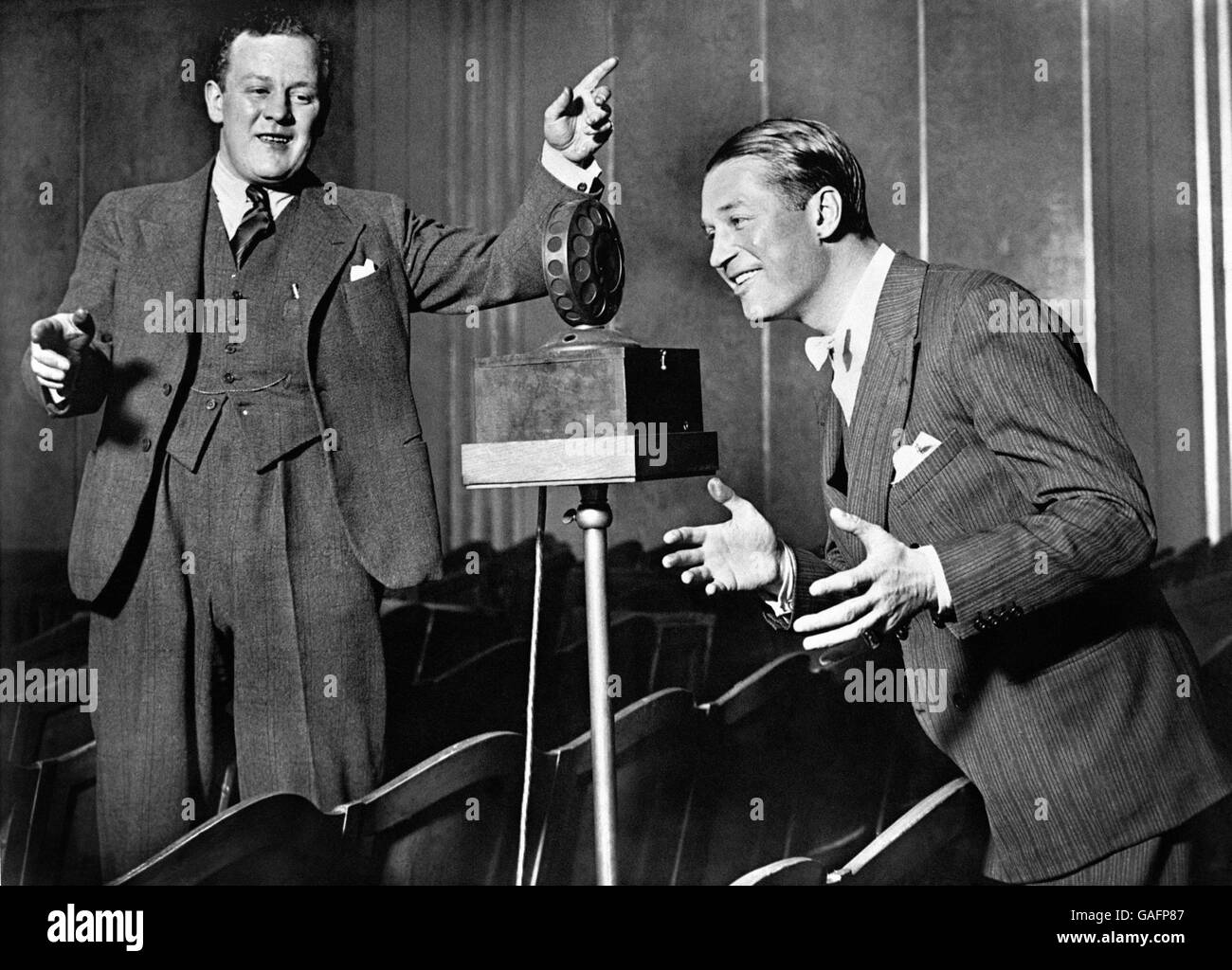 French actor and singer Maurice Chevalier in Paris singing to the microphone, with British bandleader Jack Hylton. Stock Photo
